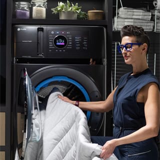 A woman pulls a duvet out of the combo washer and dryer and examines it. A woman pulls a duvet out of the combo washer and dryer and examines it.